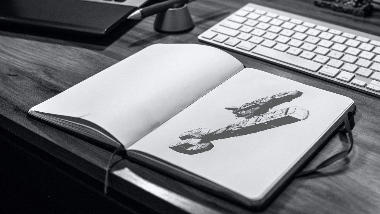 Grayscale desk scene with a spacecraft render displayed in an open sketchbook.